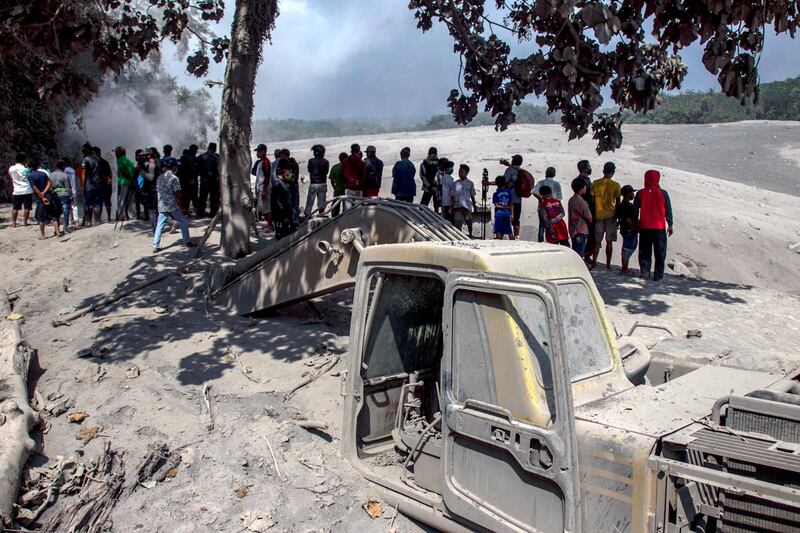 People gather near an excavator buried in volcanic, after an eruption of Mount Semeru, at a sand mining site in Lumajang, East Java, Indonesia. EPA