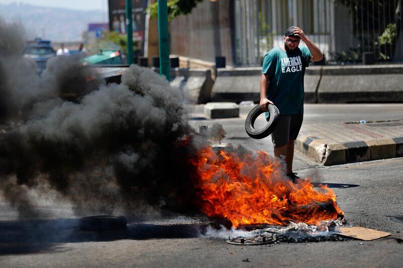 A protester burns tires, as he blocks a main highway during a protest against the increase in prices of consumer goods and the crash of the local currency, in Beirut, Lebanon, Thursday, June 17, 2021. Shops, government offices, businesses and banks shut their doors Thursday in response to a call for a general strike by Lebanon's main labor union. (AP Photo/Hussein Malla)