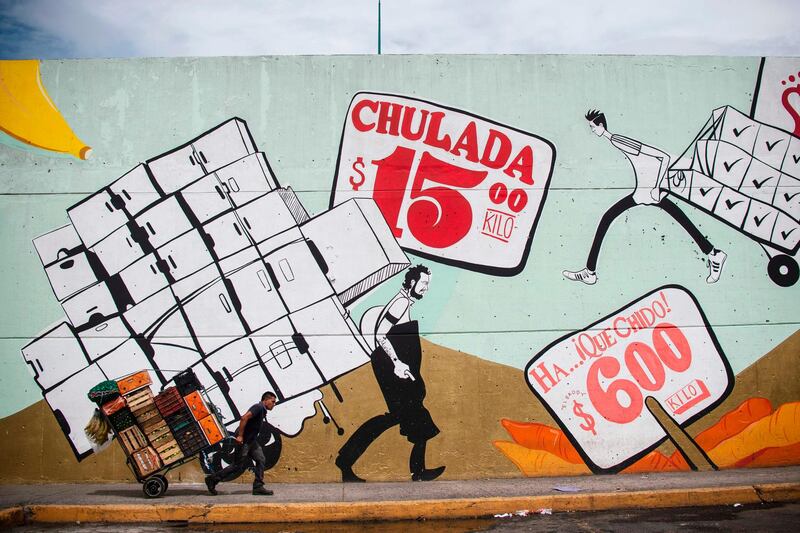 A worker pulls a cart past a mural by US artist Scarlett Baily, painted in the framework of the project "La Bodega de Arte", at the "Central de Abasto" wholesale market in Mexico City. Pedro Pardo / AFP Photo