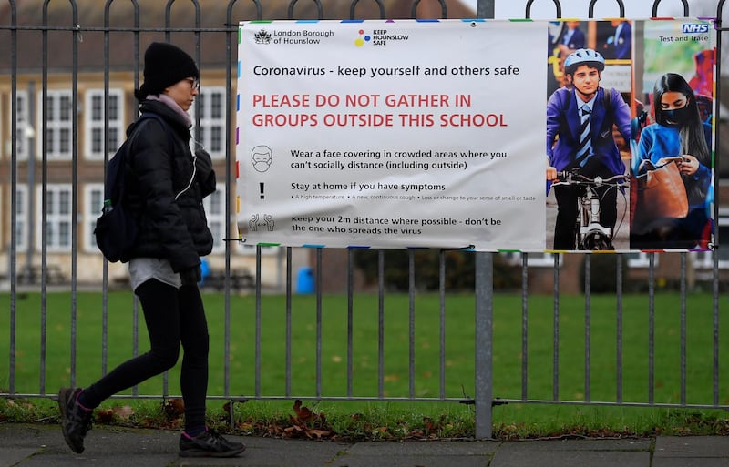 A woman walks past a social distancing health message outside of a secondary school in London, Britain December 29, 2020. REUTERS/Toby Melville