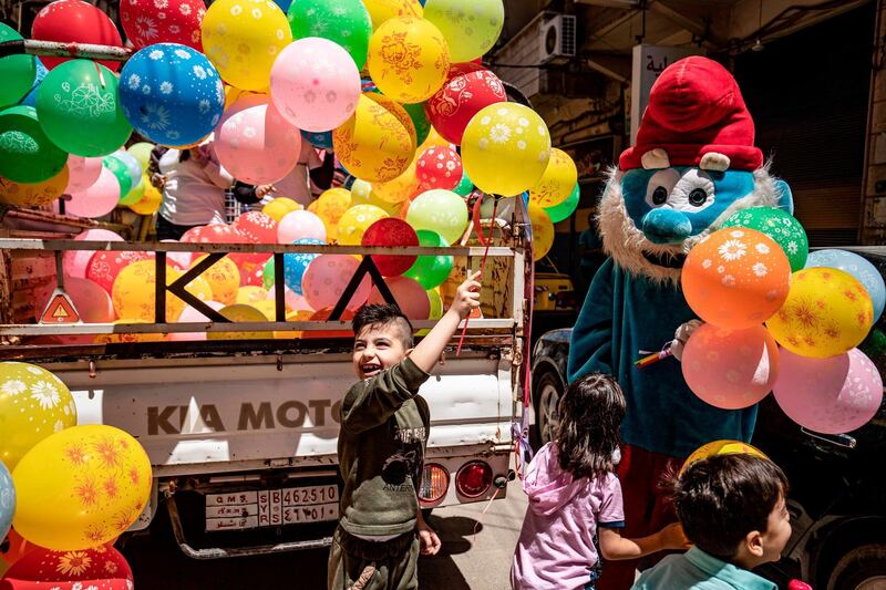 A mascot dressed as a Smurf hands balloons to children during the Eid Al Fitr holiday as part of a local awareness campaign to encourage hand-washing, hygiene, and social distancing as part of protection efforts against the coronavirus pandemic, in the Kurdish-majority city of Qamishli, in Syria's northeastern Hasakeh province. AFP