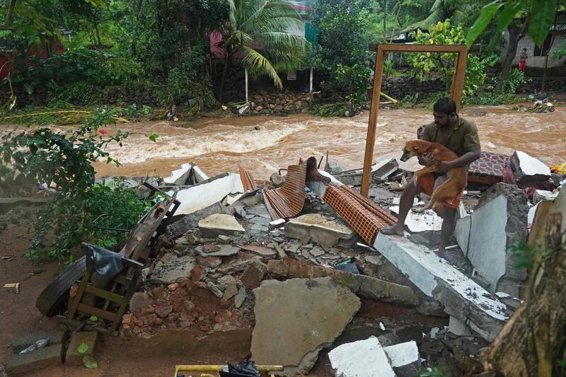 A resident carries a dog from the debris after his house was destroyed by flash floods in Thodupuzha. AFP