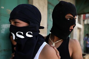 Palestinian youths wearing balaclavas take cover while hurling stones at an Israel Defense Force (IDF) checkpoint in the West Bank city of Hebron, 5 June, 2020. EPA