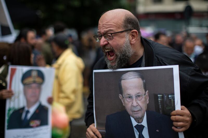 An anti-government protester holds a picture of Lebanese President Michel Aoun as he shouts slogans during a protest, in Beirut's Ashrafieh district, Lebanon, Thursday, Nov. 26, 2020. Dozens of protesters rallied Thursday outside the house of Judge Fadi Sawwan, the lead judicial investigator into the catastrophic blast at Beirut's port in August the blast that killed nearly 200 people, wounded more than 6,000 and caused billions of dollars in damage. (AP Photo/Hassan Ammar)
