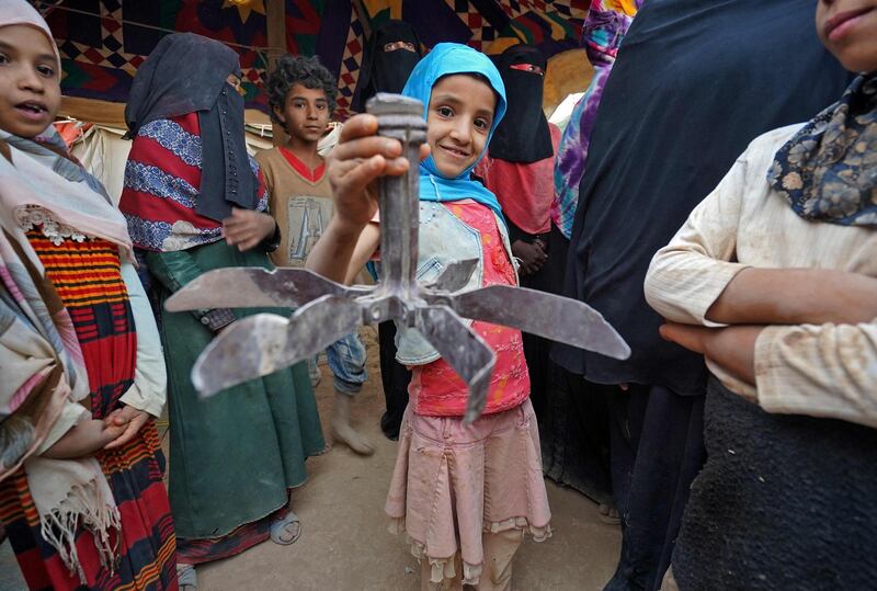 A girl holds propeller debris as she stands near other women and children by tents at the Suweida camp for people internally displaced by conflict, near Yemen's northern city of Marib. AFP