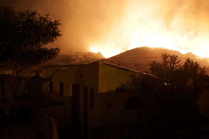 A man uses a garden hose to water the roof of a house as a wild fire rages nearby in the outskirts of Obidos, Portugal. Armando Franca / AP Photo
