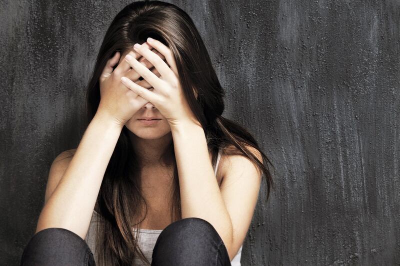 A studio shot of a sad young woman holding her head in her hands