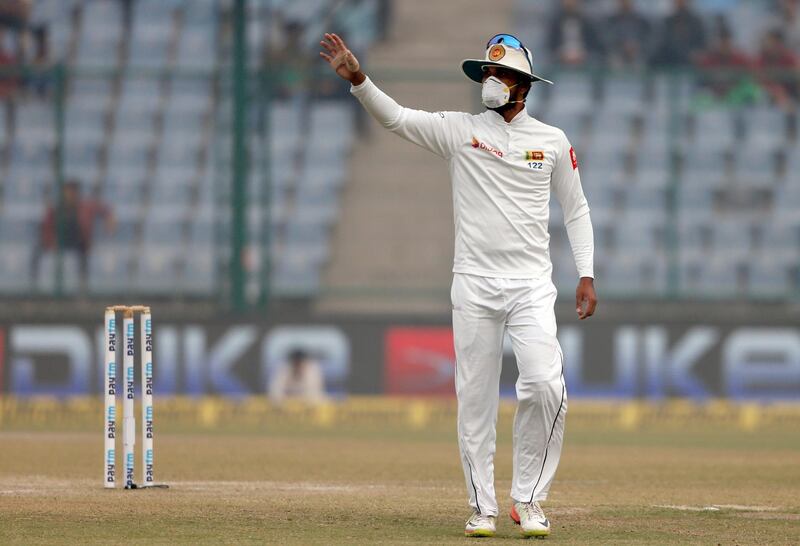 Sri Lanka's captain Dinesh Chandimal, wearing anti-pollution mask, gestures to his teammates during the fourth day of their third test cricket match against India in New Delhi. Altaf Qadri / AP Photo