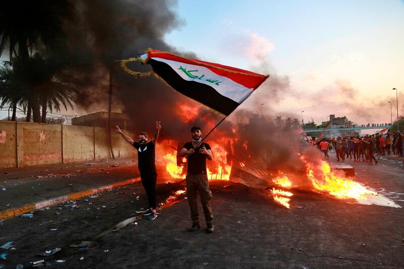 An anti-government protester waves a national flag during a demonstration in Baghdad, Iraq, Thursday, Oct. 3, 2019. Iraqi security forces fired live bullets into the air and used tear gas against a few hundred protesters in central Baghdad on Thursday, hours after a curfew was announced in the Iraqi capital on the heels of two days of deadly violence that gripped the country amid anti-government protests that killed several people in two days. (AP Photo/Hadi Mizban)
