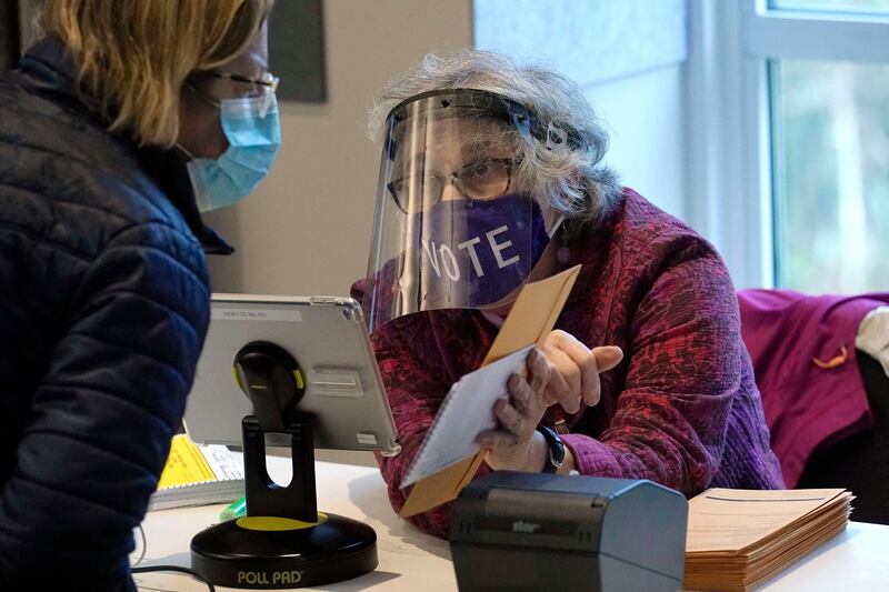 Poll worker Alice Machinist, of Newton, Mass., right, wears a mask and shield out of concern for the coronavirus while assisting a voter, left, with a ballot during early in-person general election voting, at the Newton Free Library, in Newton, Massachusetts. AP Photo