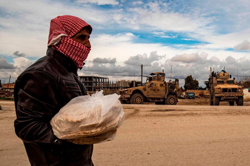 A man carrying bags of bread walks as a patrol of US military vehicles is seen in the town of Tal Tamr in the northeastern Syrian Hasakeh province along the border with Turkey.   AFP