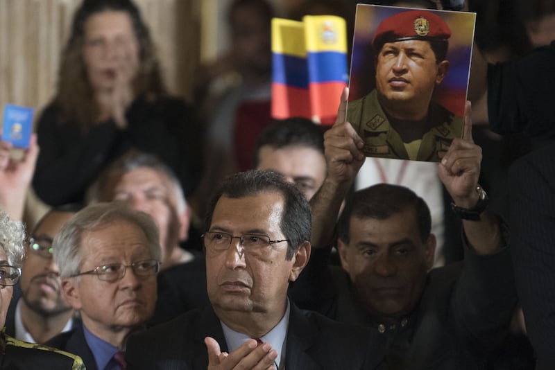 Adan Chavez, Venezuela's culture minsiter, center, sits in front of a lawmaker holding a photograph of his brother, late Venezuelan president Hugo Chavez, during a Constituent Assembly ceremony in Caracas, Venezuela, on Friday, Aug. 4, 2017. Venezuela's newly convened and widely reviled��assembly��that will rewrite the constitution selected as its leader��Delcy Rodriguez, a former foreign minister and fiery ally of President��Nicolas Maduro. Photographer: Carlos Becerra/Bloomberg