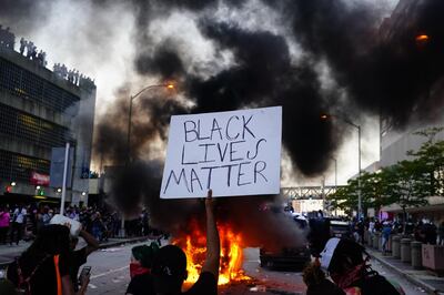 (FILES) In this file photo a man holds a Black Lives Matter sign as a police car burns during a protest on May 29, 2020 in Atlanta, Georgia. When Ridley Scott and Kevin Macdonald created documentary "Life in a Day" a decade ago, their goal was to construct a video portrait of a typical 24 hours on Earth, as filmed by tens of thousands of amateurs around the world. Repeating the trick in "Life in a Day 2020," stitching together footage shot last summer as the coronavirus pandemic and massive anti-racism protests turned the world on its head, their sequel is anything but typical. Assembled by a vast team of editors from 324,000 clips, the film -- which premieres February 1, 2021, at Sundance before hitting YouTube -- captures the eerily empty streets, collective cabin-fever and civil unrest of a year like no other. / AFP / GETTY IMAGES NORTH AMERICA / Elijah Nouvelage
