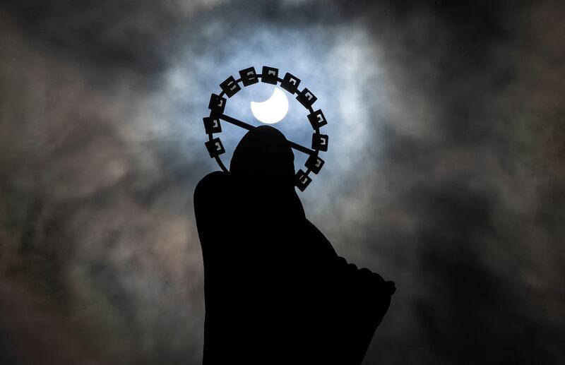 A statue of Our Lady, Star Of The Sea on Bull Wall in Dublin, is silhouetted against the sky during a partial solar eclipse. PA via AP
