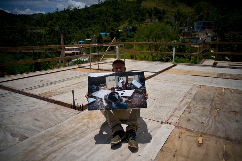 Luis Cosme poses on the roof of his new home as he holds a printed photo taken on October 1, 2017 showing him on his property destroyed by Hurricane Maria.