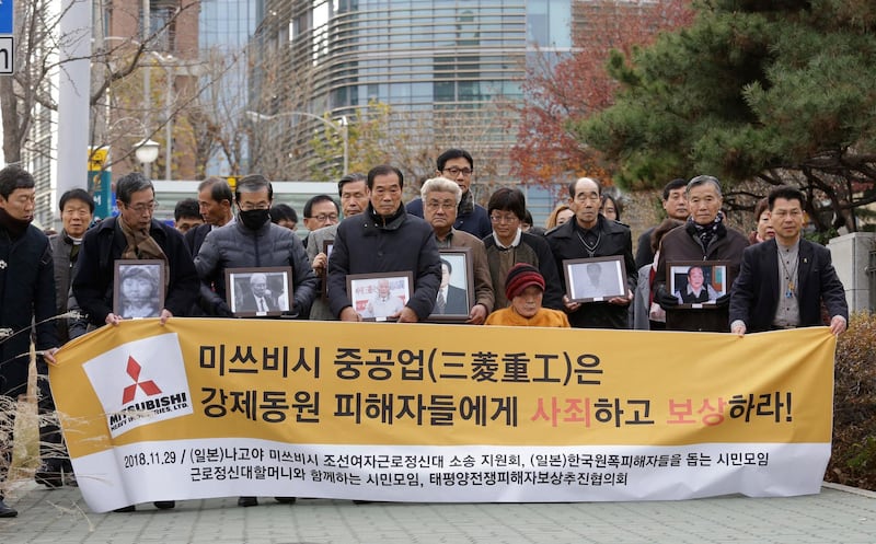 FILE - In this Nov. 29, 2018, file photo, victims of Japan's forced labor and their family members arrive at the Supreme Court in Seoul, South Korea. Colonial-era Korean laborers on Tuesday, July 16, 2019, are seeking a court's approval for the sales of local assets of their former Japanese employer after it refused to comply with a court order to compensate them for forced labor decades ago. The sign reads "Mitsubishi Heavy Industries should compensate and apologize to victims of forced labor." (AP Photo/Ahn Young-joon, File)