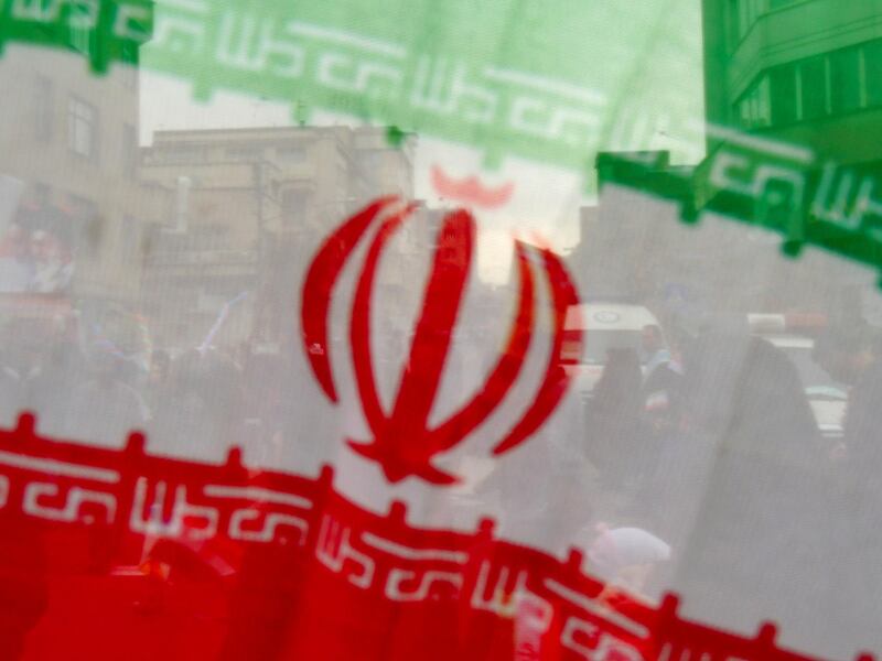Wavy and slanted Iranian flag in the front plane, with masses of Iranian people behind who celebrate an anniversary of the 1979 Islamic Revolution and Iranian independence day, in a march along Azadi avenue toward Azadi square every 22nd of Bahman or 10-11th of February.