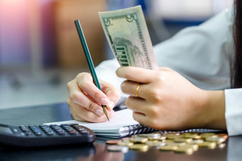 Close up hand female with pencil writing on the book and hand hold US dollar. Calculation at home