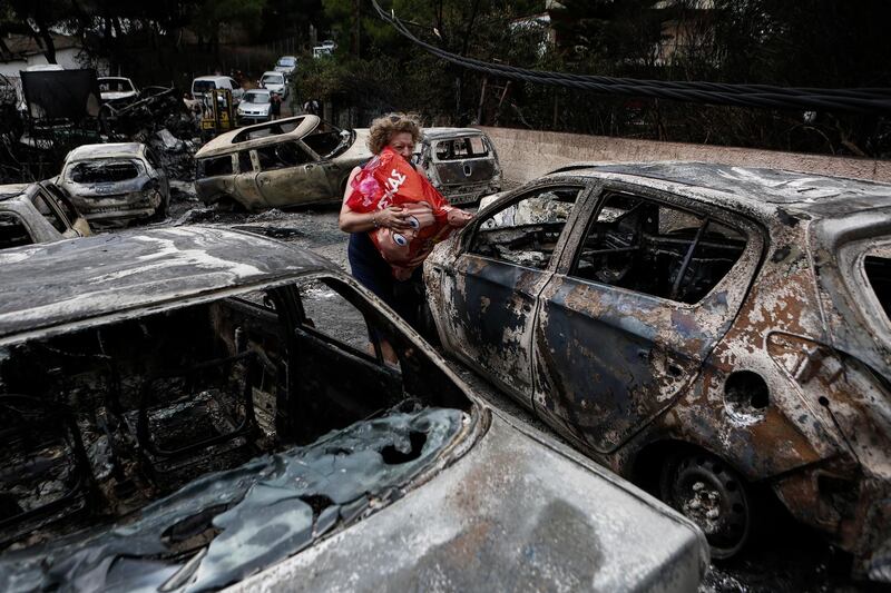 epa06907587 A woman carries her belongings amidst burned cars following a forest fire in Mati a northeast suburb of Athens, Greece, 24 July 2018. At least 50 people have lost their lives in wildfires that broke out in eastern Attica while there are fears of even more casualties, as many telephone calls have been made to the Fire Brigade to report missing persons.  EPA/YANNIS KOLESIDIS