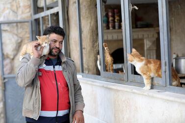 Mohammed Alaa al-Jaleel carries a cat on his shoulder at Ernesto's Cat Sanctuary that he runs in Kfar Naha, an opposition-held town in Aleppo province in Syria on March 17, 2018. The 43-year-old, al-Jaleel who grew up in Aleppo, has been mad about cats since he was a boy. As the war raged in Syria and cat lovers fled the city, he was left with 170 cats to feed and a new nickname: the Cat Man of Aleppo. / AFP / OMAR HAJ KADOUR