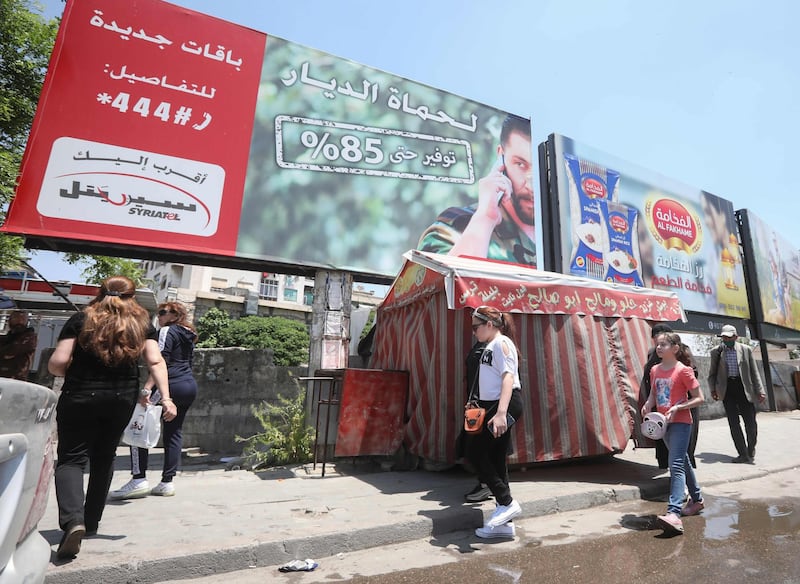 People walk underneath an advertising billboard of Syria's largest mobile operator Syriatel, owned by businessman Rami Makhlouf, in the Syrian capital Damascus on May 11, 2020. Syria's top tycoon publicly airing his grievances has revealed a power struggle within the ruling family as it tries to cement its power after nine years of war, analysts say. After years of staying out of the limelight, business magnate Rami Makhlouf this month in two videos on Facebook laid bare his struggles with the regime headed by his first cousin President Bashar al-Assad, in what analysts say is a desperate last stand. / AFP / STR
