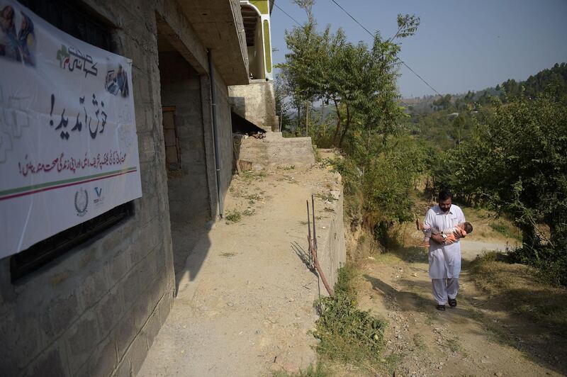 This photograph taken on October 19, 2017, a Pakistani resident carries his sick son as they arrive at an online treatment clinic in the remote Bhosa village of Mansehra district.
In a remote northern Pakistani village surrounded by lush green hills, Mohammad Fayyaz brings his two-year-old son to a clinic so that a female doctor sitting hundreds of kilometres away can examine him. / AFP PHOTO / AAMIR QURESHI / TO GO WITH: Pakistan-health-technology, FEATURE by Sajjad Tarakzai