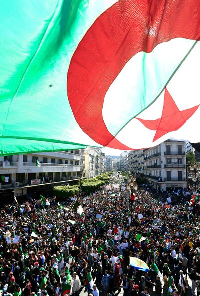 Algerians mach under a giant national flag during a protest in Algiers, Algeria, Friday, March 15, 2019. Tens of thousands of people gathered Friday in Algeria's capital and other cities amid heavy security for what could be decisive protests against longtime leader Abdelaziz Bouteflika. (AP Photo/Toufik Doudou)