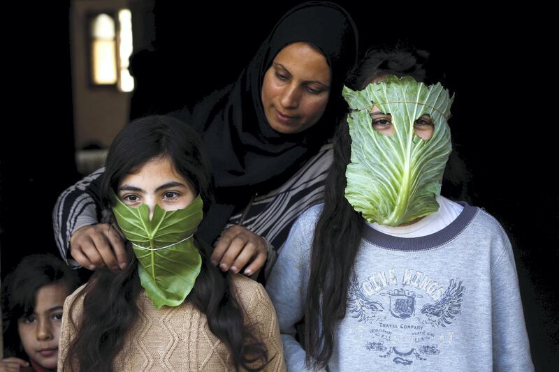 A Palestinian mother entertain her children with makeshift masks made of cabbage as she cooks in Beit Lahia in the northern Gaza Strip on April 16, 2020 amid the coronavirus COVID-19 pandemic. (Photo by MOHAMMED ABED / AFP)