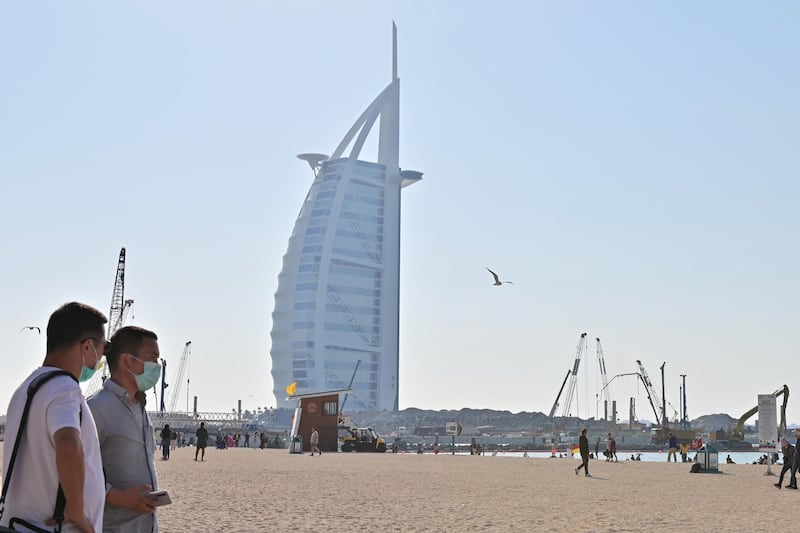 Tourists wearing surgical are pictured on a beach next to Burj Al Arab on January 29 2020. The United Arab Emirates announced the first confirmed cases of the new coronavirus in the Middle East, with a four-member Chinese family from Wuhan found to be infected. / AFP / GIUSEPPE CACACE
