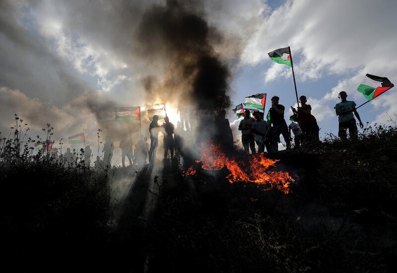 Protesters wave Palestinian Flags as tyres burn at a rally against the Israeli Flag March, in the east of the Gaza Strip. EPA