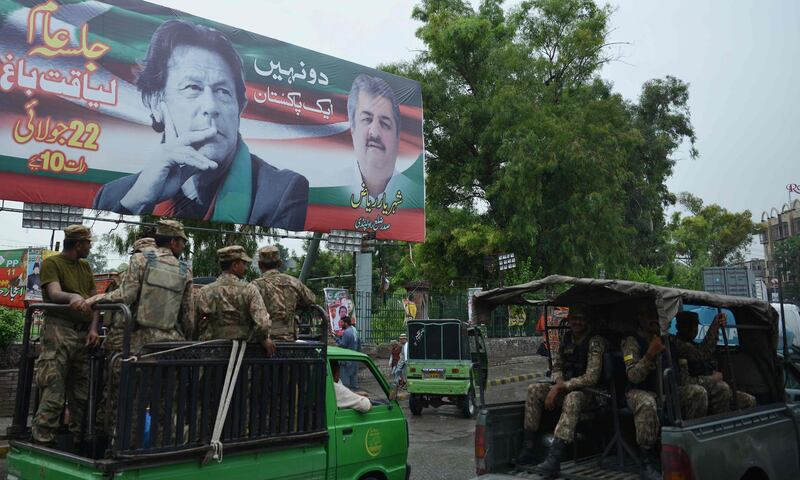 Pakistani soldiers patrol on a street beside a billboard featuring an image of Pakistani cricketer turned politician Imran Khan (top L) of the Pakistan Tehreek-e-Insaf (Movement for Justice), ahead of general election in Rawalpindi on July 23, 2018. Pakistan will hold the general election on July 25. / AFP / AAMIR QURESHI
