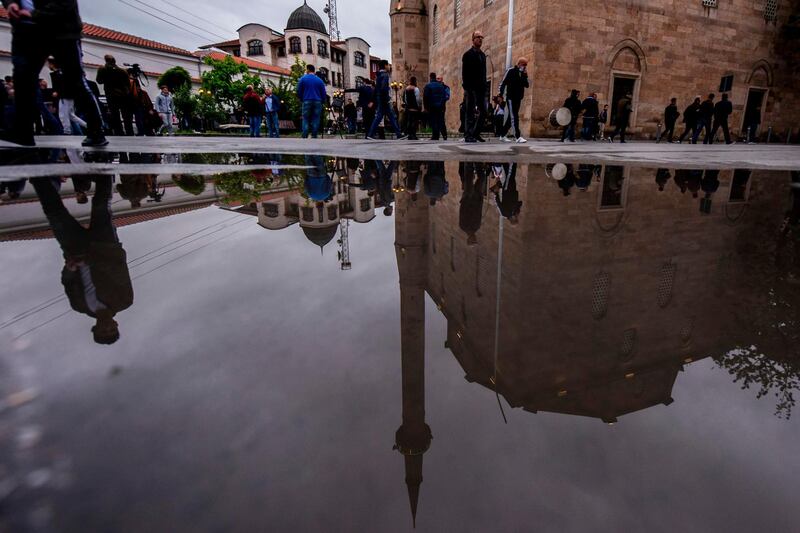 Muslim devotees are reflected in a puddle near the grand mosque in Pristina. AFP