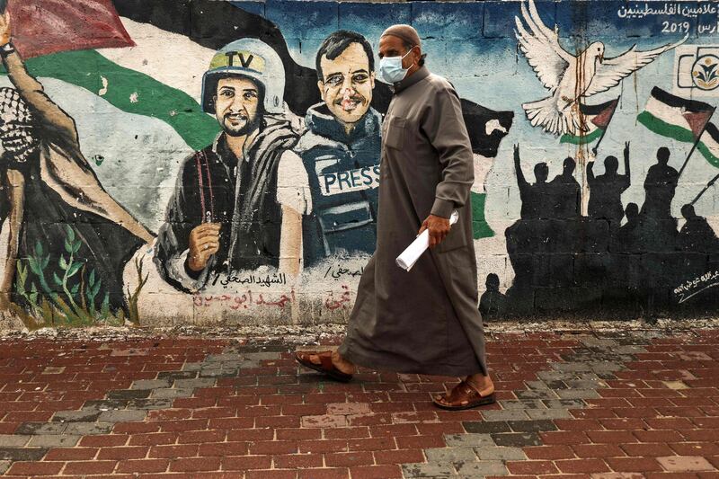 A Palestinian man wearing a face mask walks past a mural of journalists killed in 2014 between Hamas and Israel, in Gaza City. AFP