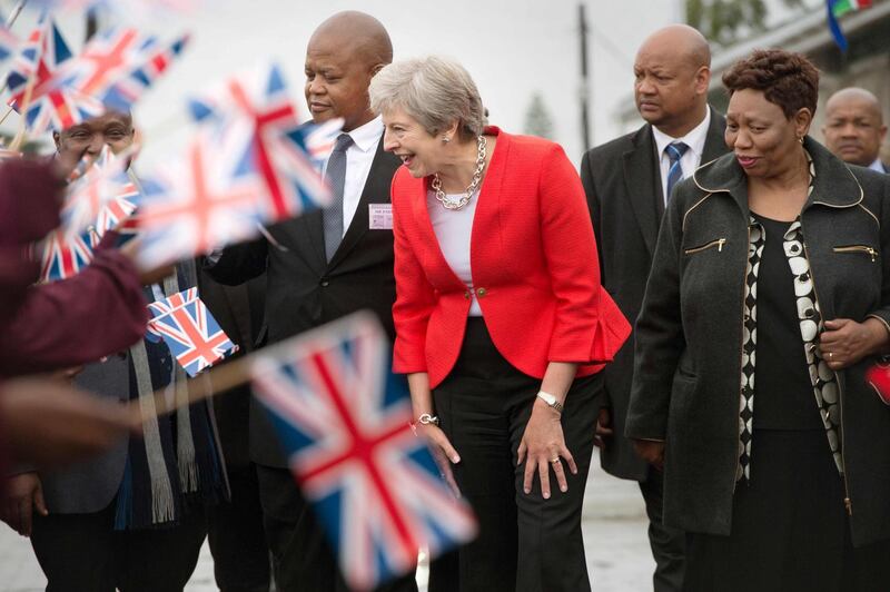 TOPSHOT - Britain's Prime Minister Theresa May (C) is greeted by schoolchildren waving British and South African flags, during a visit to the ID Mkhize Secondary School in Gugulethu township, about 15 km from the centre of Cape Town, on August 28, 2018, as part of a three-nation visit to Africa in Cape Town where she is expected to discuss post-Brexit trade ties with the continent's most developed economy. (Photo by Rodger BOSCH / POOL / AFP)