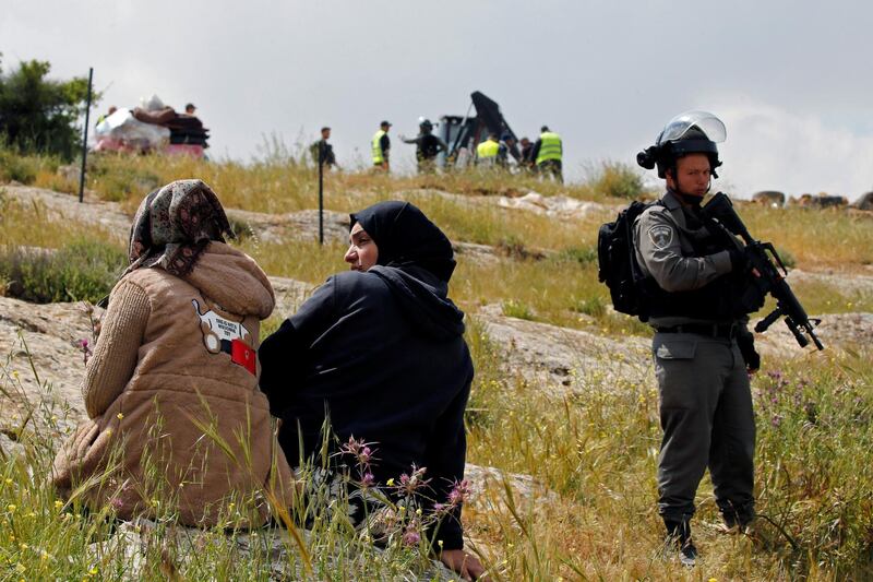 An Israeli border policeman stands guards next to Palestinians as workers guarded by Israeli forces remove a Palestinian tent whose owners said they were informed by the forces that they didn’t obtain a permit to erect the tent, in Susiya village in the Israeli-occupied West Bank. Reuters