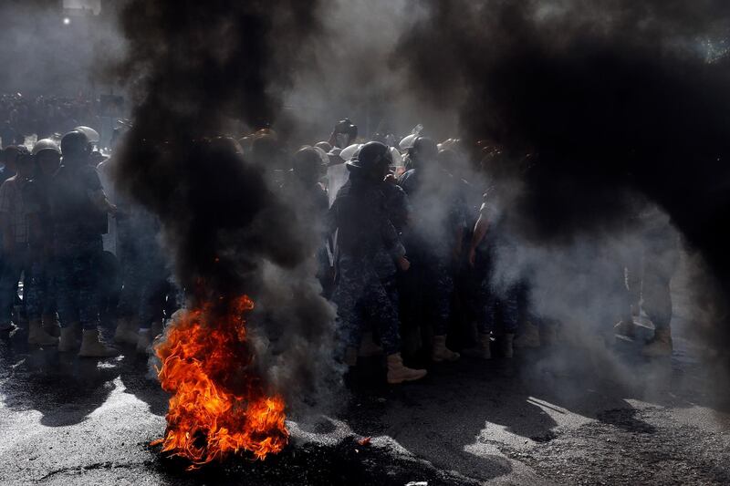 Riot police stand guard, as retired Lebanese soldiers burn tires during a protest in front of the government building, in Beirut, Lebanon.  AP Photo