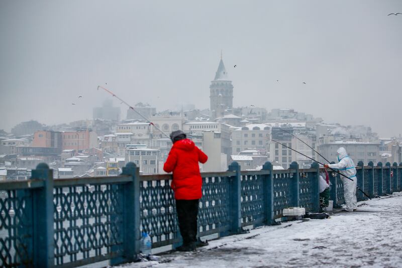 People fish in the snow on Galata Bridge over the Golden Horn waterway. AP