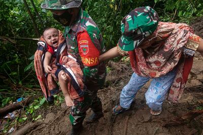 An Indonesian soldier assists a woman to carry her baby as they make their way through an area affected by earthquake-triggered landslide near Mamuju, West Sulawesi, Indonesia, Saturday, Jan. 16, 2021. Damaged roads and bridges, power blackouts and lack of heavy equipment on Saturday hampered Indonesia's rescuers after a strong and shallow earthquake left a number of people dead and injured on Sulawesi island. (AP Photo/Yusuf Wahil)