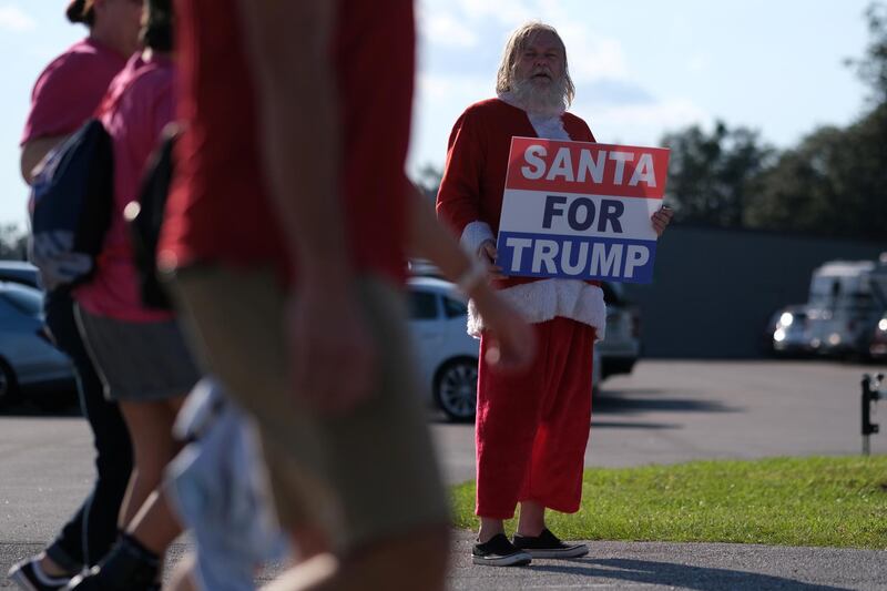A man dressed as Santa Claus holds a sign as supporters of U.S. President Donald Trump arrive for an election campaign rally at Orlando Sanford International Airport in Sanford, Florida, U.S. REUTERS
