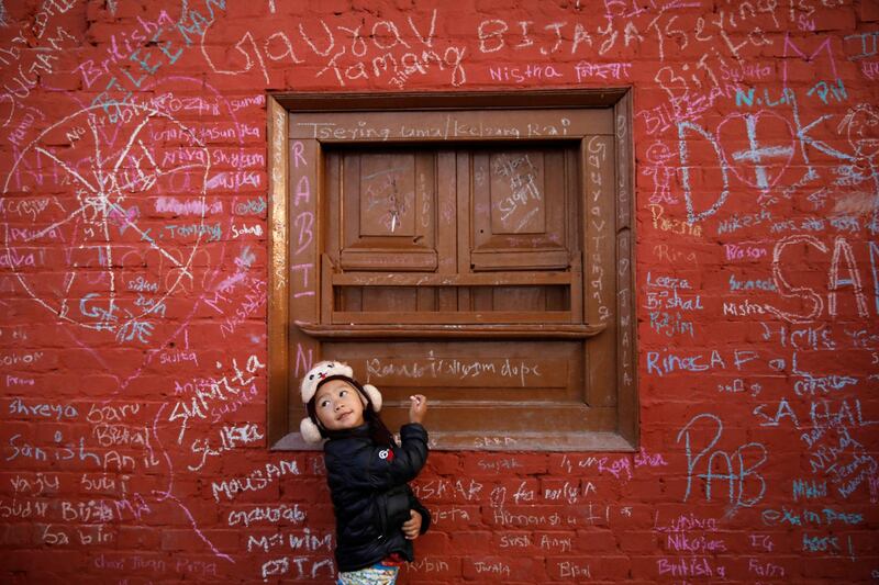 A girl looks towards her father as she writes on the wall of a Saraswati temple during the Shreepanchami festival in Kathmandu, Nepal. Reuters