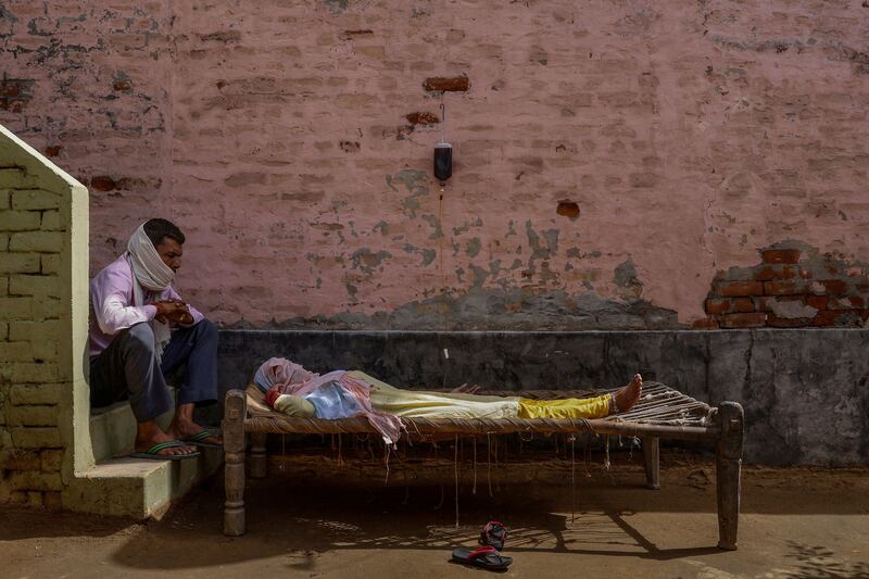 A man sits next to his wife as she receives rehydration fluid at a makeshift clinic during a surge of the coronavirus disease in Parsaul village, in the state of Uttar Pradesh, India, on May 22, 2021. By Adnan Abidi, Pulitzer Prize Winner for Feature Photography.  Reuters