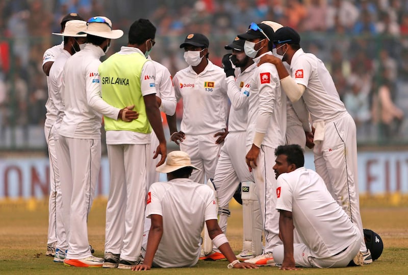 Sri Lanka's players, wearing anti-pollution masks, speak to each other as the game was briefly stopped during the second day of their third test cricket match in New Delhi. Altaf Qadri / AP Photo