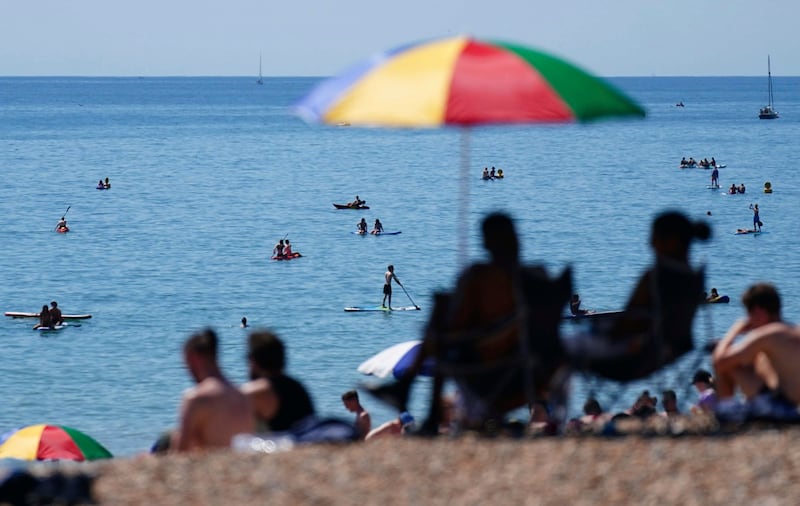 People gather on the beach while others cool off in the shallows during hot weather at Brighton, southern England. AP
