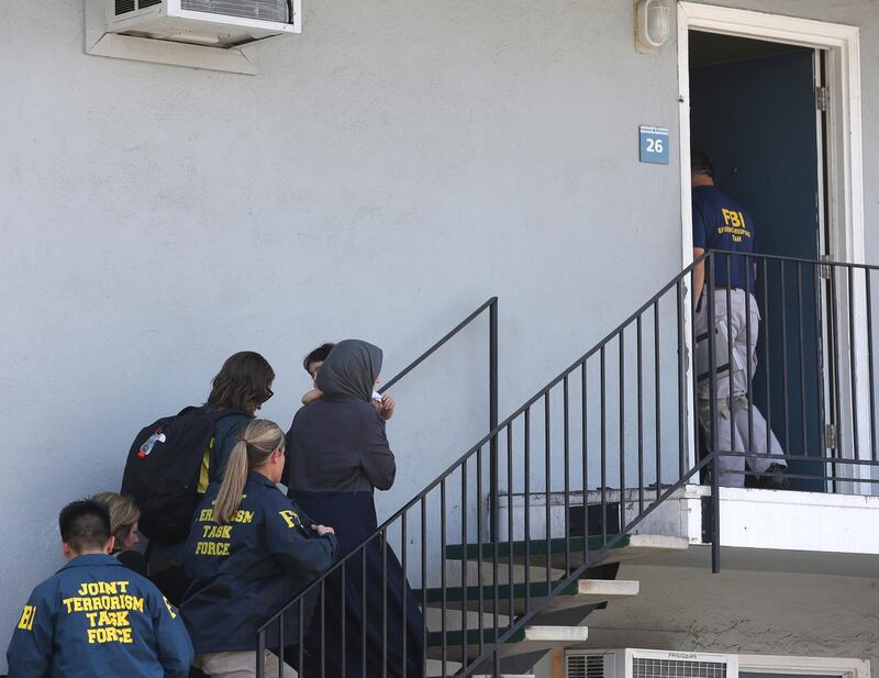 A woman carrying a child is escorted by authorities to an apartment following the arrest of a 45-year-old Iraqi refugee, Omar Ameen, Wednesday, Aug. 15, 2018, in Sacramento, Calif. Ameen was arrested on a warrant alleging that he killed an Iraqi policeman in 2014 while serving with the Islamic State terror organization. (AP Photo/Rich Pedroncelli)