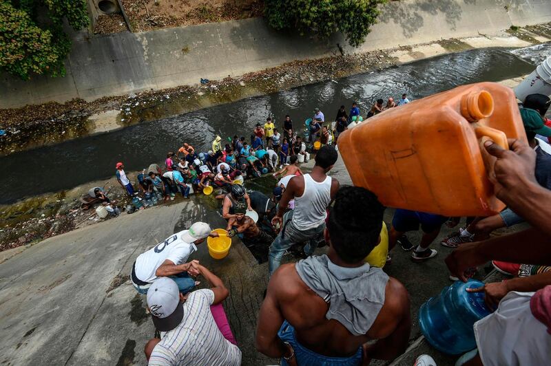 People collect water from a sewage canal at the river Guaire in Caracas, Venezuela, as a massive power outage continues affecting some areas of the country. AFP