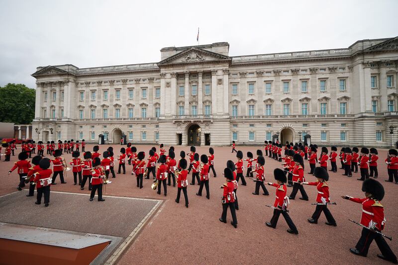 British soldiers in scarlet tunics and bearskin hats parade outside Buckingham Palace. PA