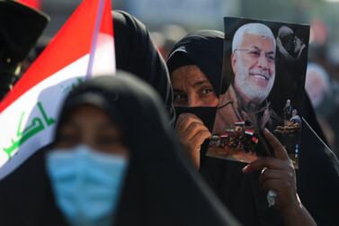 TOPSHOT - An Iraqi demonstrator lifts a portrait of slain Iraqi commander Abu Mahdi al-Muhandis during a rally in Tahrir square in the capital Baghdad on January 3, 2021, to mark one year after a US drone strike killed him alongside Iran's revered commander Qasem Soleimani near the capital. Thousands of Iraqi mourners chanted "revenge" and "no to America", one year after the US strike which killed Soleimani and al-Muhandis and brought Washington and Tehran to the brink of war in early 2020, an anniversary that was also marked in recent days across Iran and by supporters in Syria, Lebanon, Yemen and elsewhere. / AFP / AHMAD AL-RUBAYE
