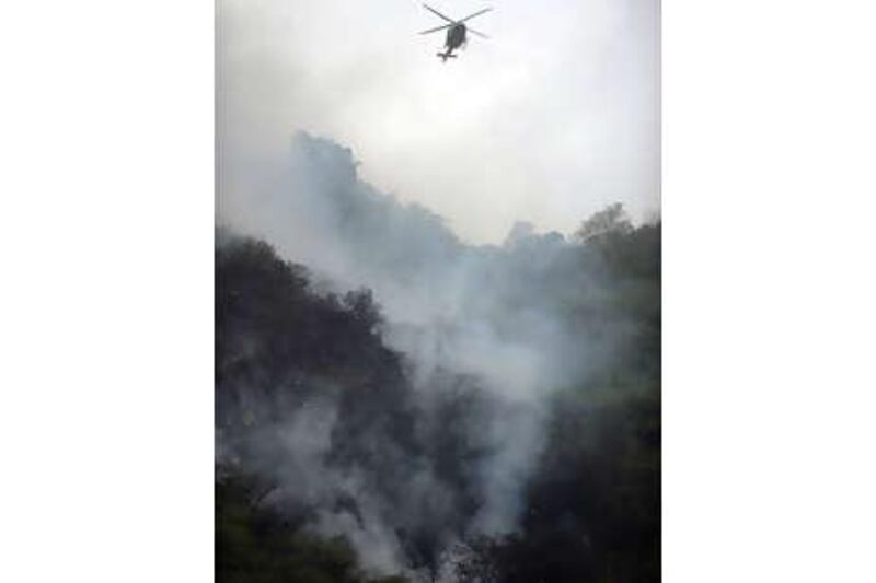 A Pakistani rescue helicopter flies over smoke and wreckage of a crashed passenger plane in The Margalla Hills on the outskirts of Islamabad on July 28, 2010.  A Pakistani passenger plane with 150 people on board crashed in a ball of flames in densely wooded hills while trying to land in Islamabad during bad weather, aviation officials said. AFP PHOTO/AAMIR QURESHI