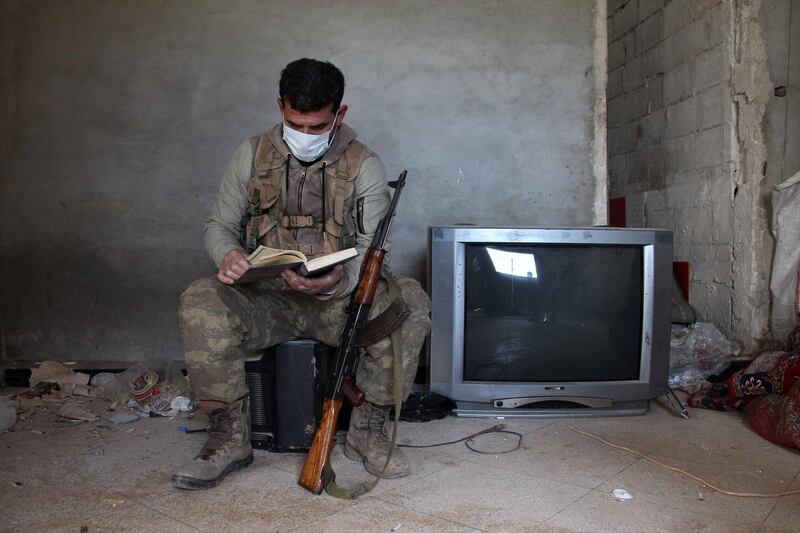 A Turkey-backed Syrian fighter wearing a face mask flips through a book as he rests at a position in the village of Aafes, north of the city of Saraqib in the northwestern Idlib province, during the coronavirus pandemic. AFP