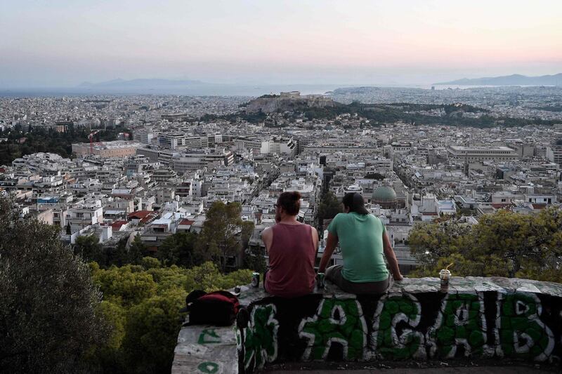 Young men sit at a hill overlooking the city of Athens on August 8, 2018. - On August 20, Greece's third and final bailout officially ends after years of hugely unpopular and stinging austerity measures. The economy is growing slowly, and unemployment fell to below 20 percent in May for the first time since 2011. (Photo by Louisa GOULIAMAKI / AFP)